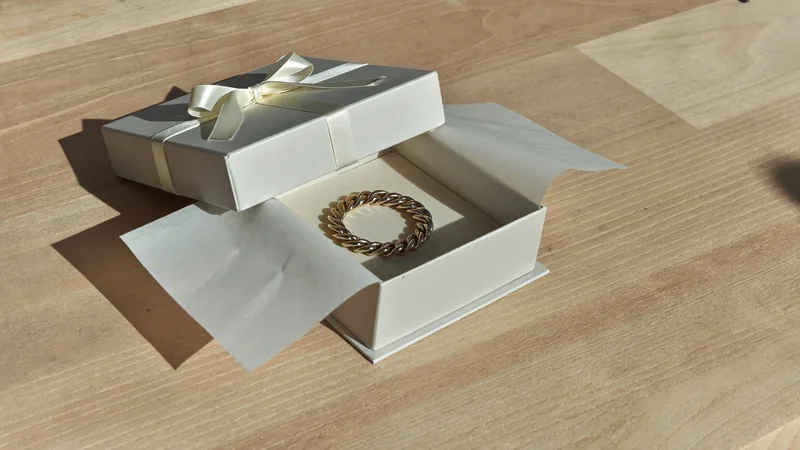 Graue Geschenkbox mit Satinband, geöffnet, mit Armband auf Seidenpapier auf hellem Holztisch